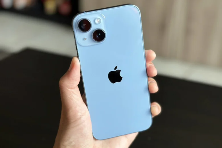 Синій iPhone у руці людини на фоні розмитого інтер'єру.